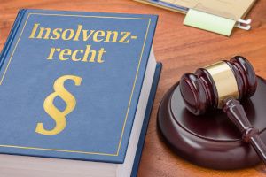 Ein dickes Gesetzbuch mit dem Aufdruck "Insolvenzrecht" liegt auf einem Tisch. Rechts daneben liegt ein Richterhammer